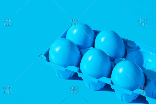 Blue painted eggs in a blue carton on blue background