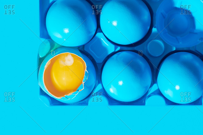 Blue painted eggs on blue background with one broken