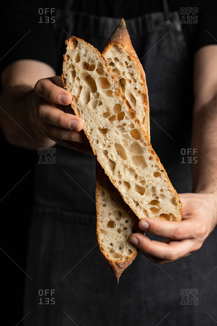Unrecognizable crop male cook in apron with tasty crunchy baguette in bakery