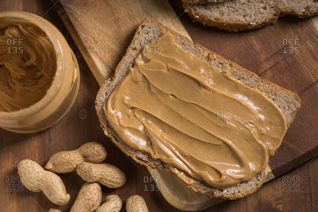 Top view of piece of bread with creamy peanut butter placed on wooden table in kitchen