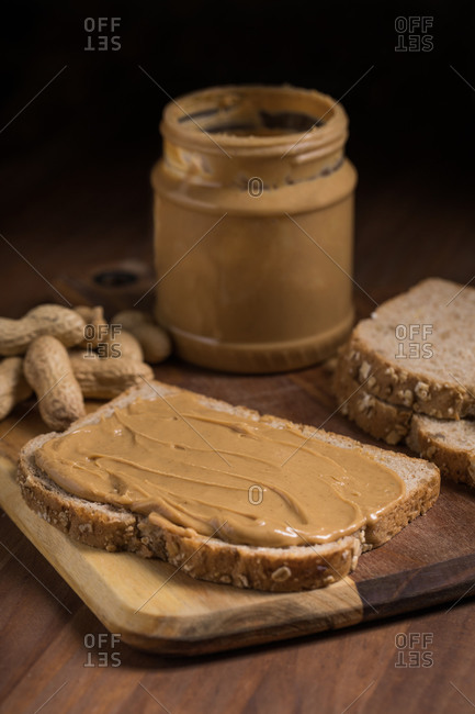 Piece of bread with creamy peanut butter placed on wooden table in kitchen