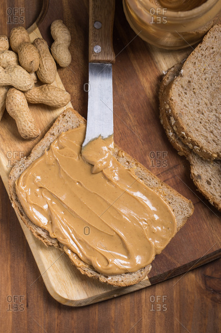 Top view of piece of bread with creamy peanut butter placed on wooden table in kitchen