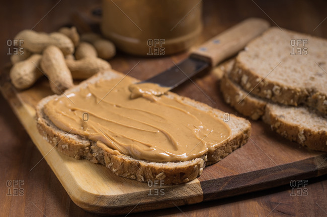 Piece of bread with creamy peanut butter placed on wooden table in kitchen