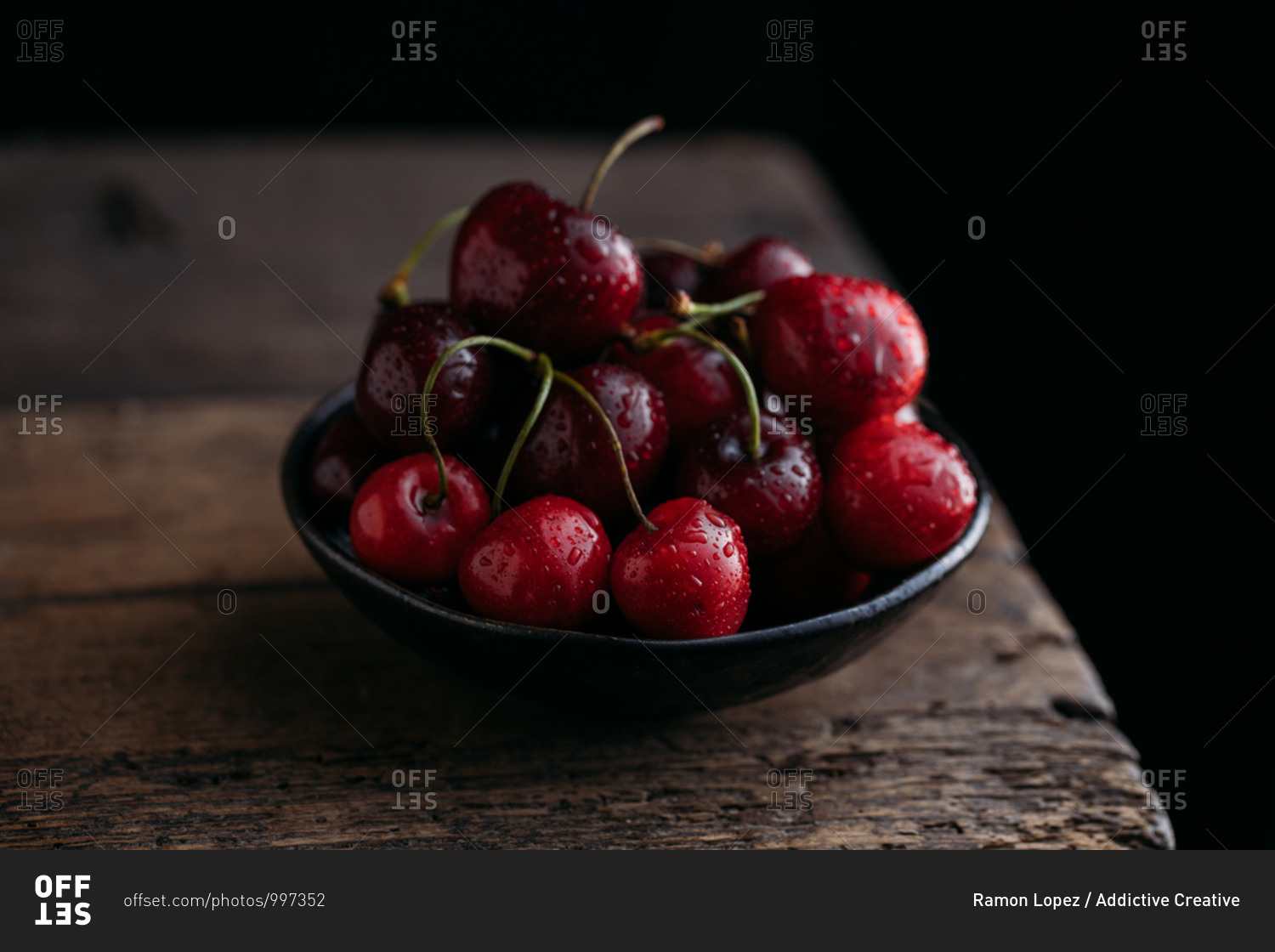 Bow full of fresh cherries on wooden table against dark background