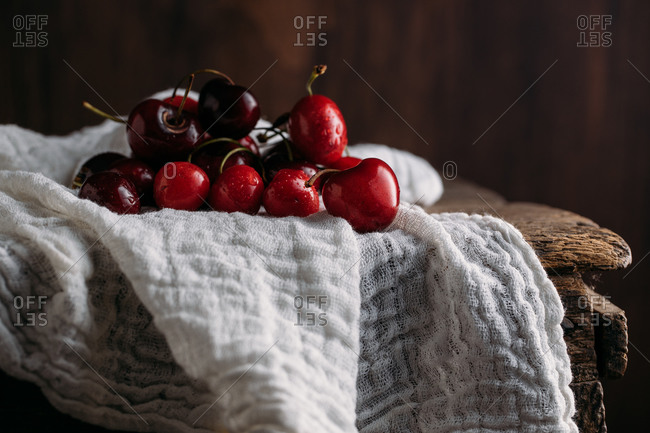 Bow full of fresh cherries on wooden table and white muslin fabric against dark background