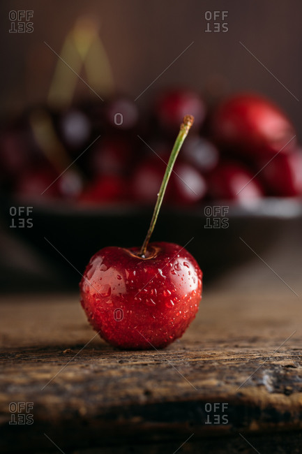 Close up view of cherry, on the background bowl full of fresh cherries on wooden table against dark background