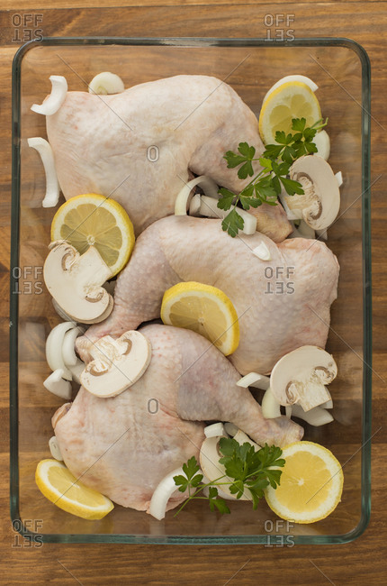Uncooked chicken with tomatoes lemon and mushrooms in glass oven recipient resting on a wooden table