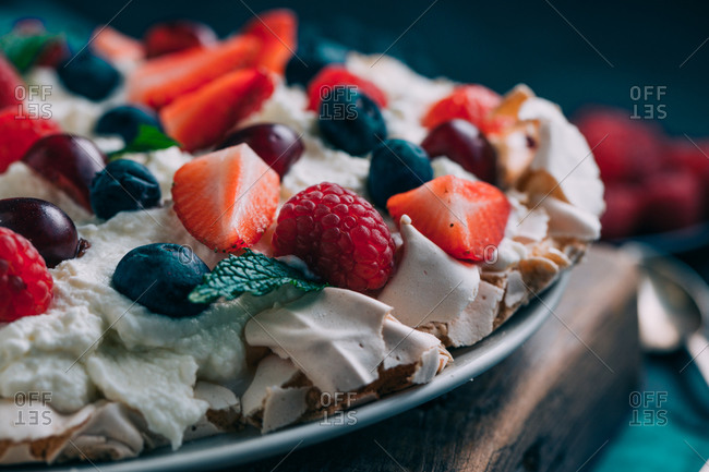 Delectable sweet meringue Pavlova cake with assorted fresh berries including strawberry and raspberry with cherry and blueberry served on table with berries and flowers