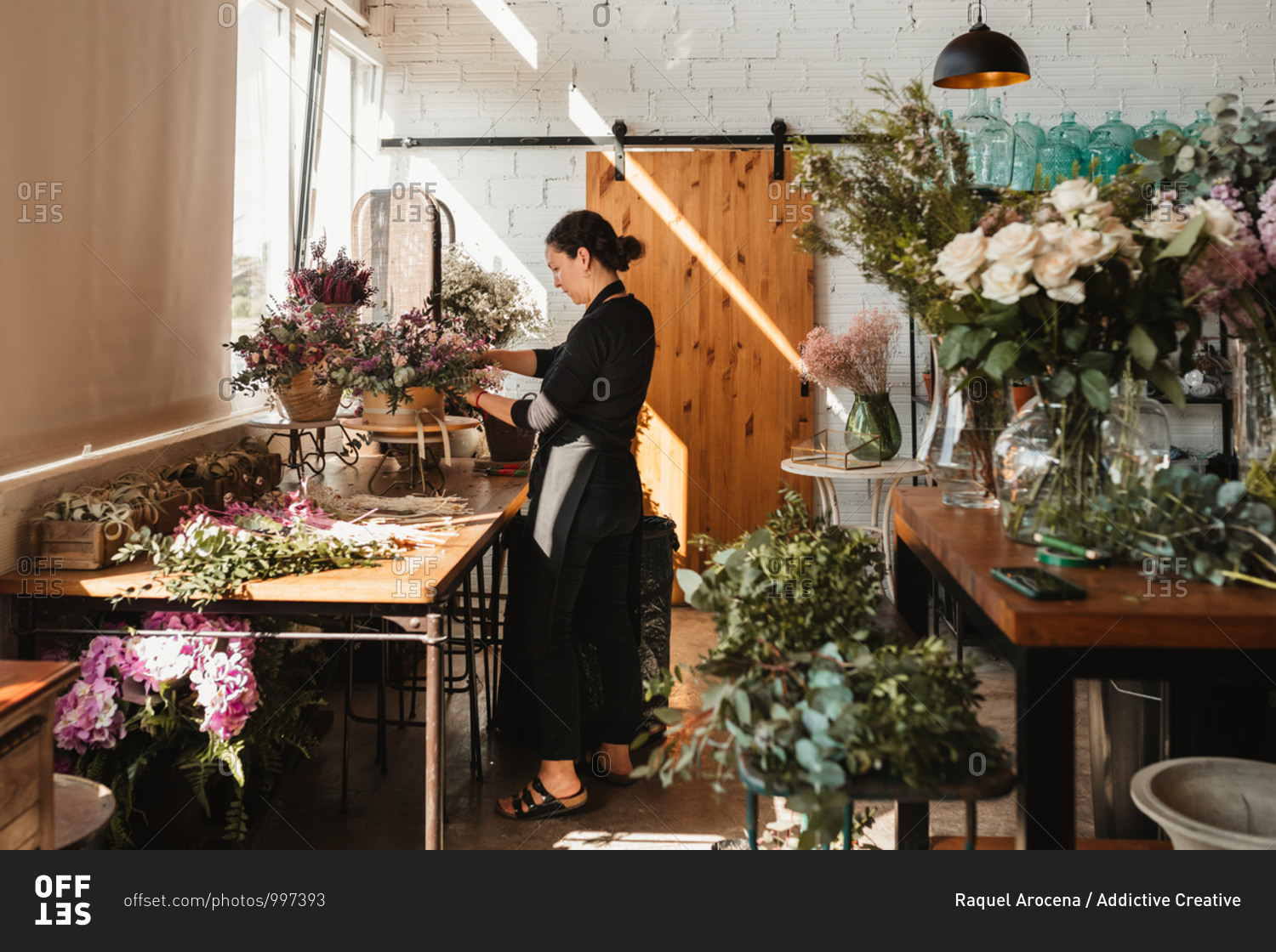 Side view of concentrated female designer arranging decorative blooming bouquets while working on order for event in creative floristry studio