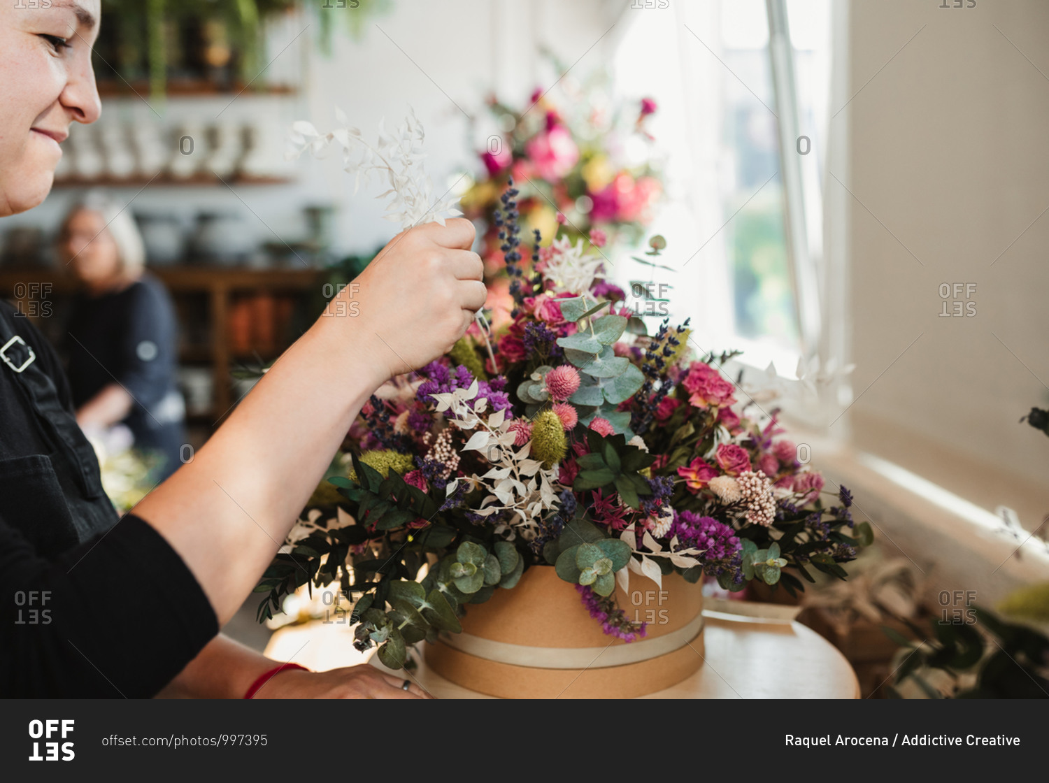 Crop of side view of concentrated female designer arranging decorative blooming bouquets while working on order for event in creative floristry studio