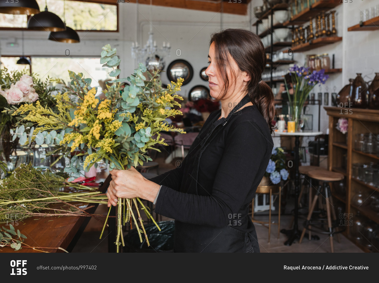 Side view of concentrated female designer arranging decorative blooming bouquets while working on order for event in creative floristry studio