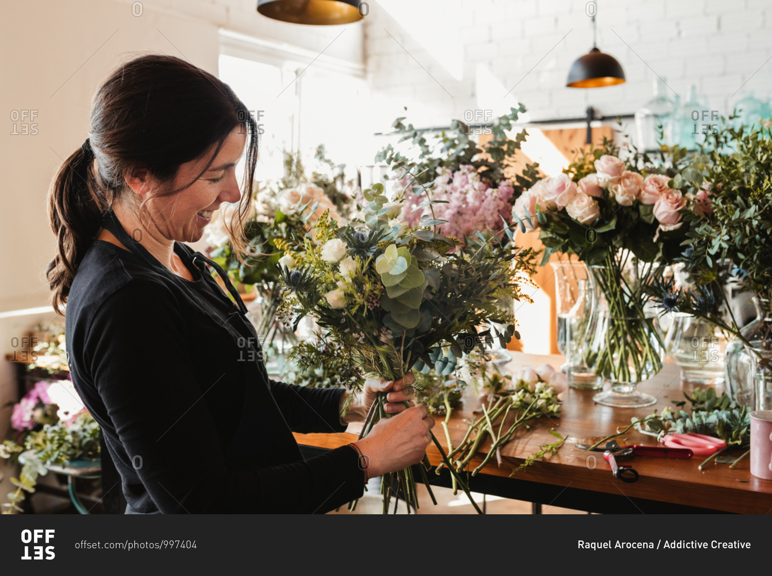 Side view of happy female designer arranging decorative blooming bouquets while working on order for event in creative floristry studio