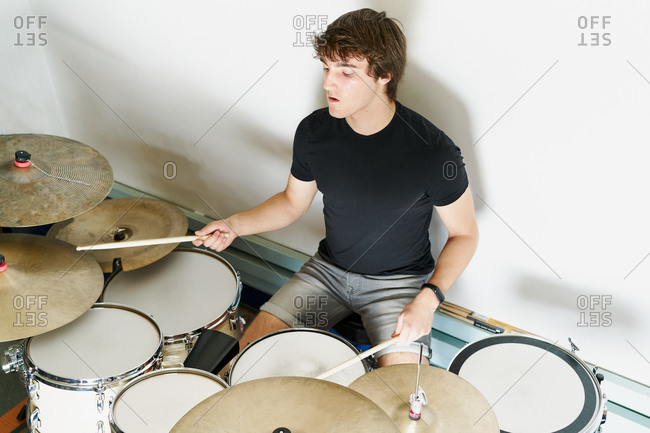 From above calm focused male drummer playing on drum kit sitting on white background stage