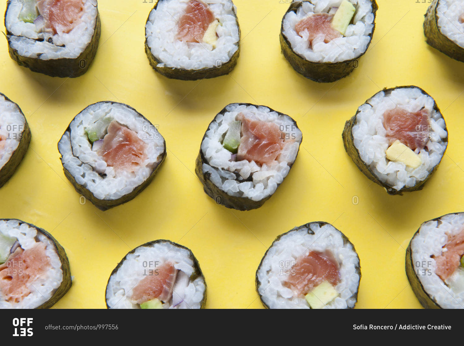 Top view of delicious sushi rolls with rice and salmon placed on colorful yellow table with chopsticks in studio