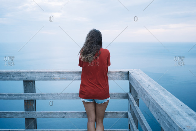 Back view of hipster woman while standing on wooden observation deck against ocean shore
