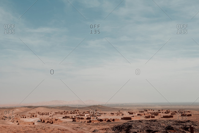 Distant small village located in dry desert terrain under cloudy blue sky in Morocco