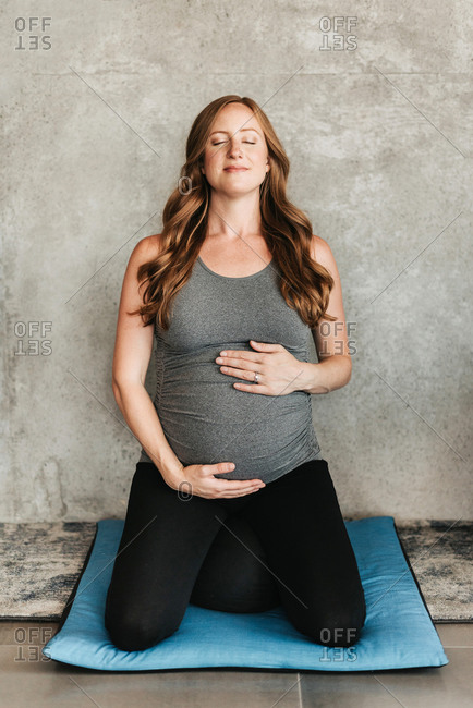 Pregnant woman on yoga mat beside concrete wall