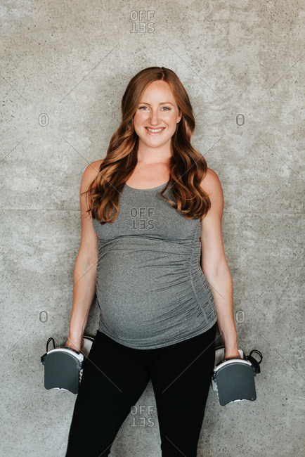 Pregnant woman with weights beside concrete wall