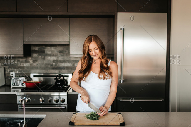 Pregnant woman preparing salad on cutting board in kitchen