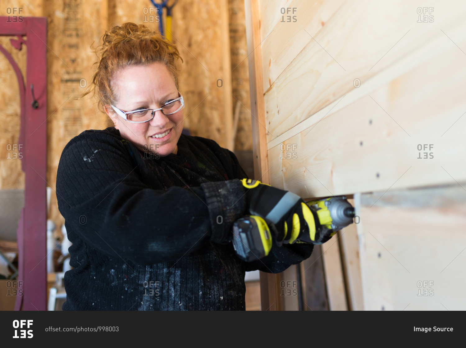Mature female carpenter using power drill in workshop