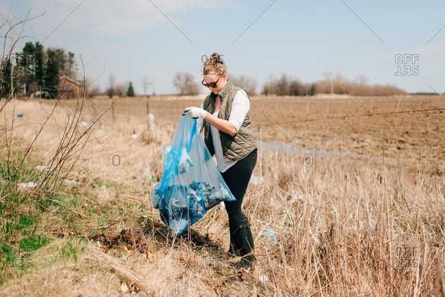 Woman picking up rubbish by field, Georgetown, Canada