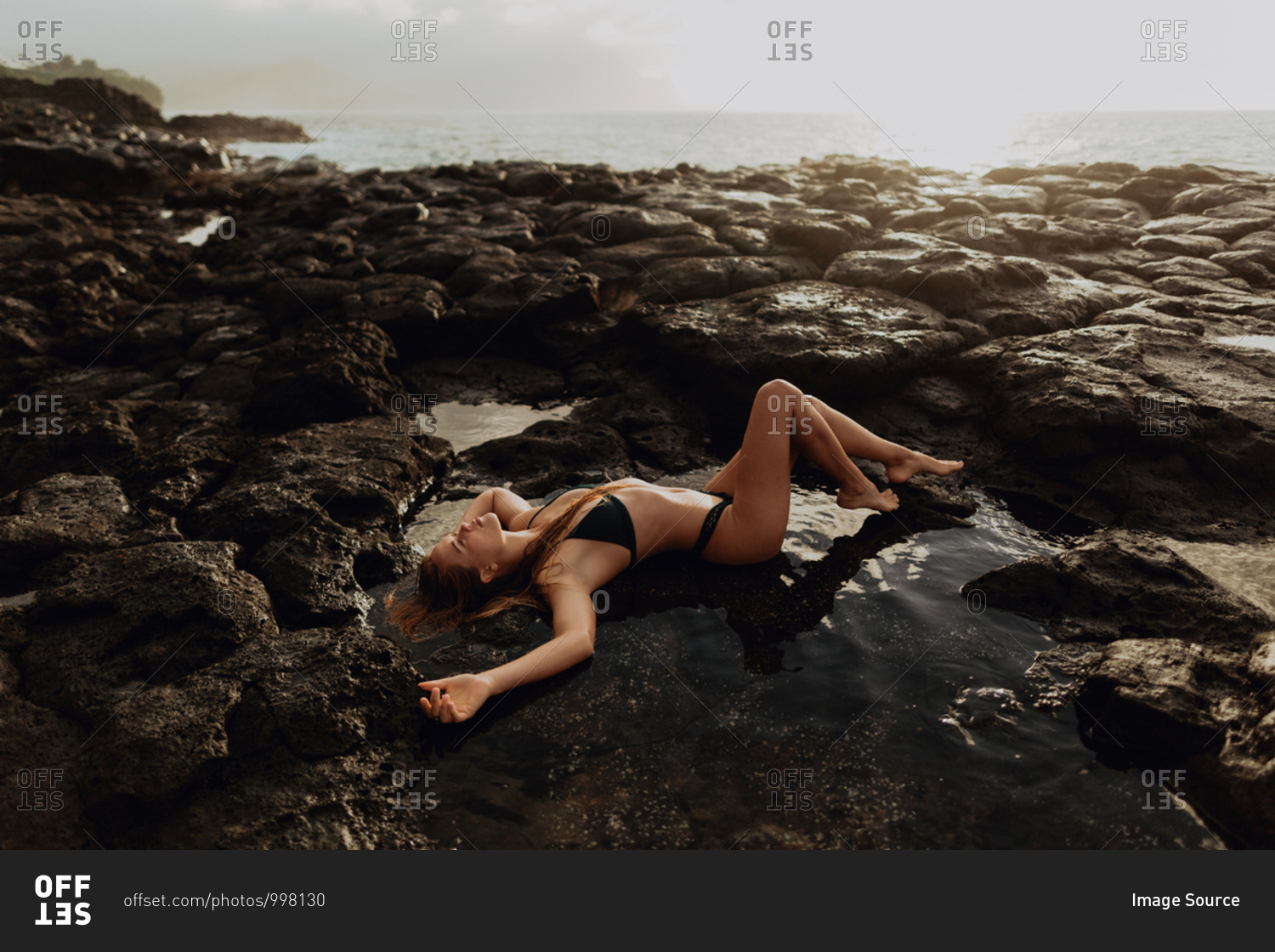 Woman lying on rocks by seaside, Princeville, Hawaii, US
