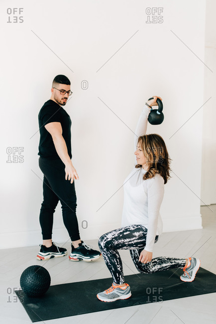 Woman practicing kettlebell squat with personal trainer at gym