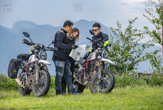 Bikers checking map next to off road motorcycles, mountains in background, Chiang Mai, North Thailand