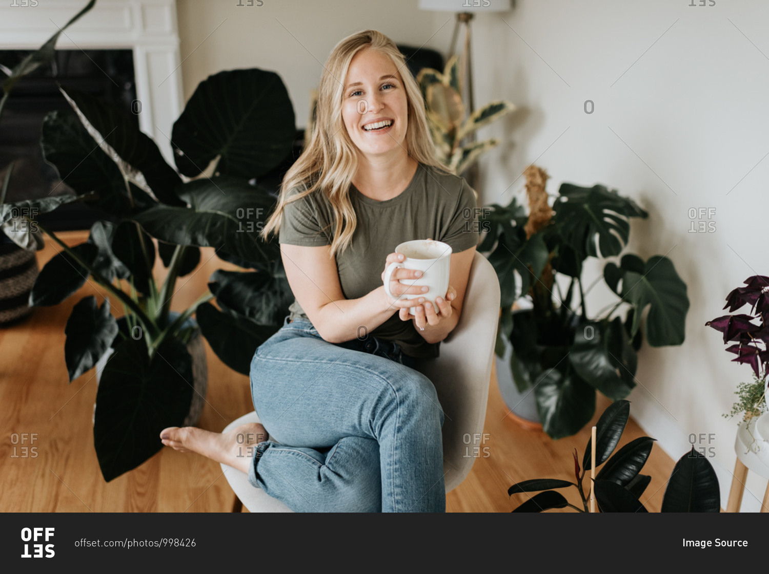 Woman relaxing with warm beverage in room full of house plants