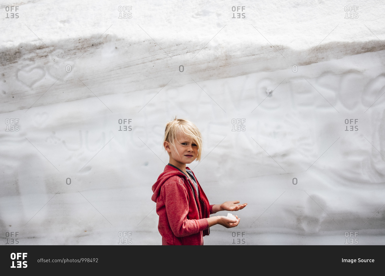Child playing with snow in front of wall with scribblings