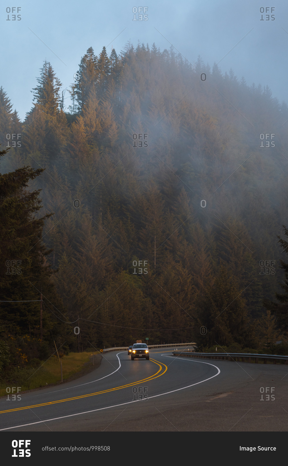 Vehicles driving down windy road on foggy afternoon along coast, Redwood forest, California, USA
