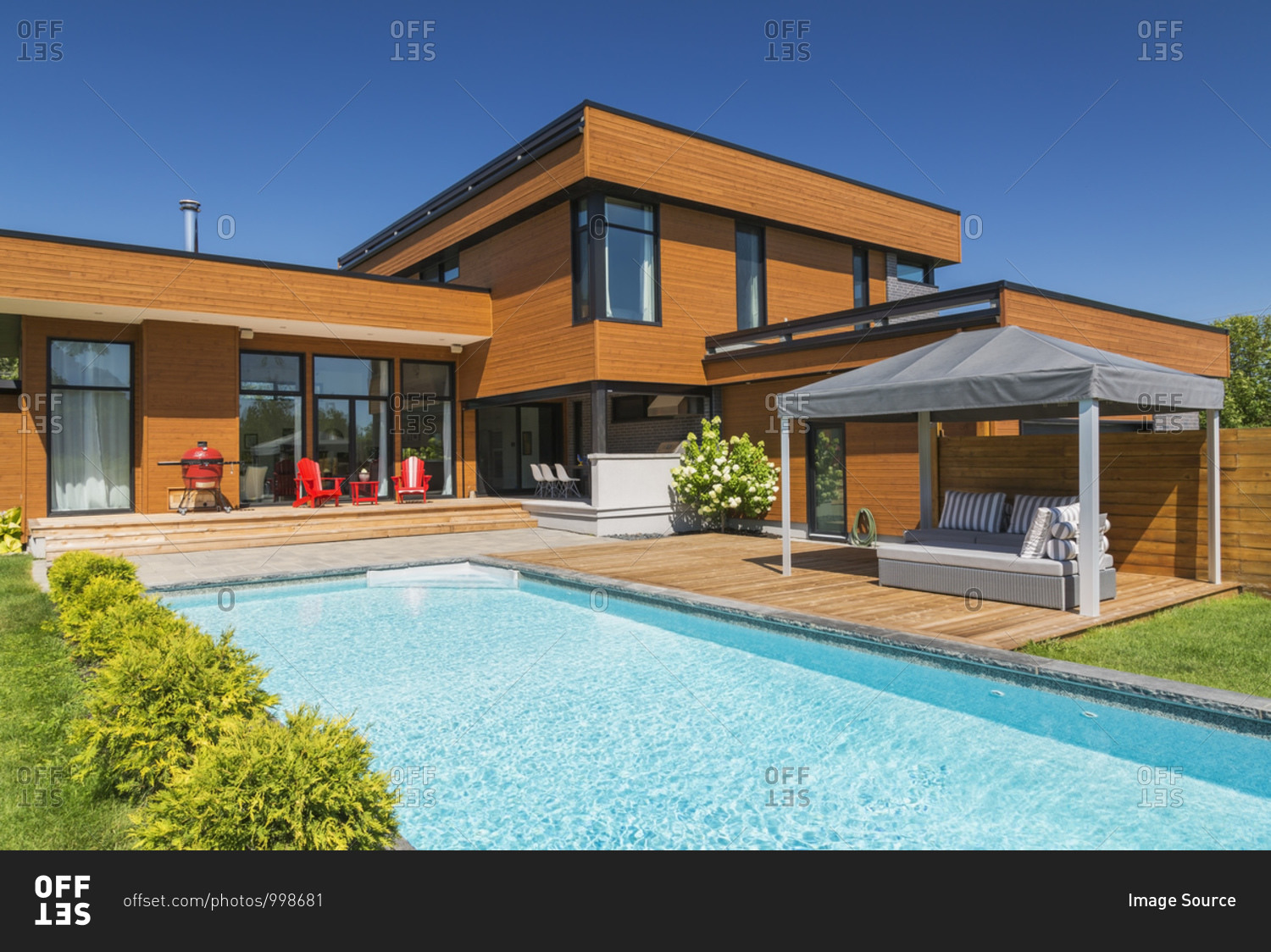 Exterior view of modern cube style home with stained horizontal wood cladding, swimming pool and wooden deck with gazebo canopy, Quebec, Canada.