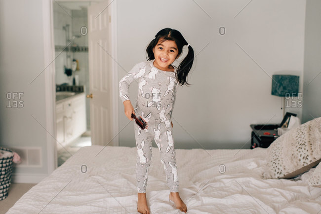 Girl with hairbrush standing on bed, portrait