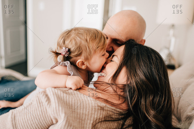 Mother and father reclining on bed together with baby daughter, over the shoulder view