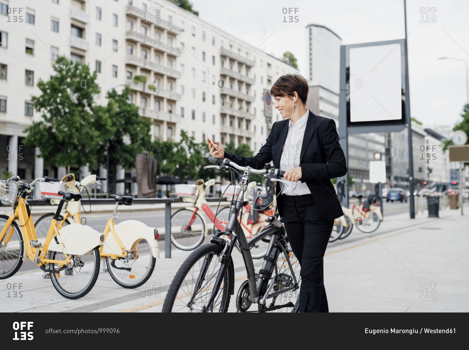 Businesswoman listening music while walking with bicycle on sidewalk in city
