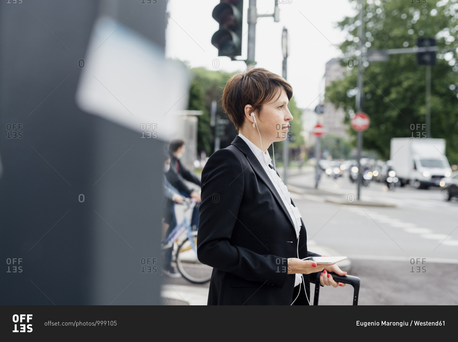 Businesswoman listening music through headphones looking away while standing on street in city