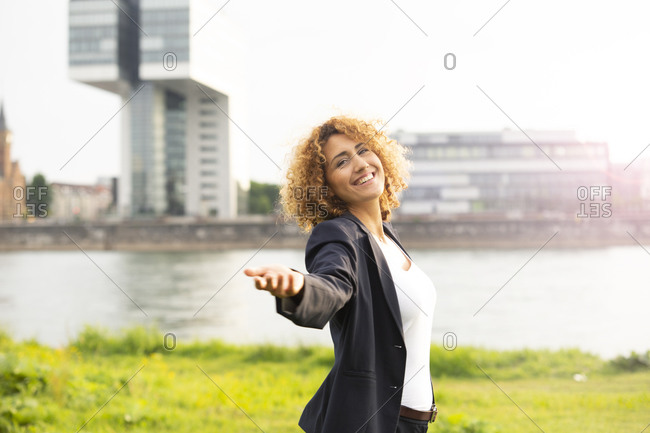 Smiling businesswoman with arm outstretched standing against river in city