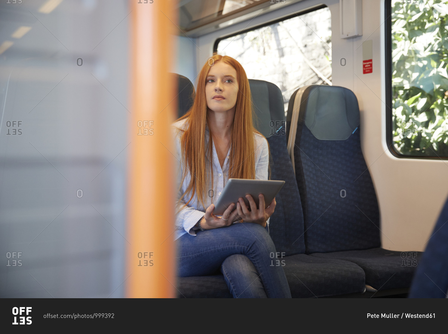 Thoughtful young woman holding digital tablet while sitting in train