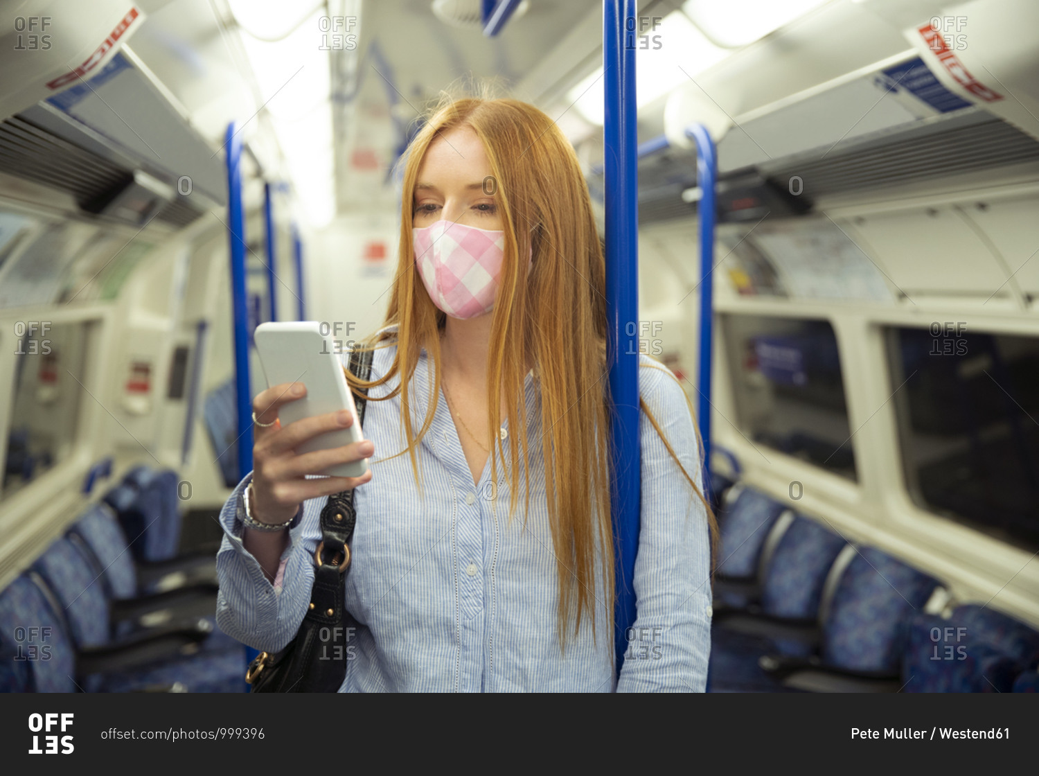 Young woman in mask using smart phone while standing in train