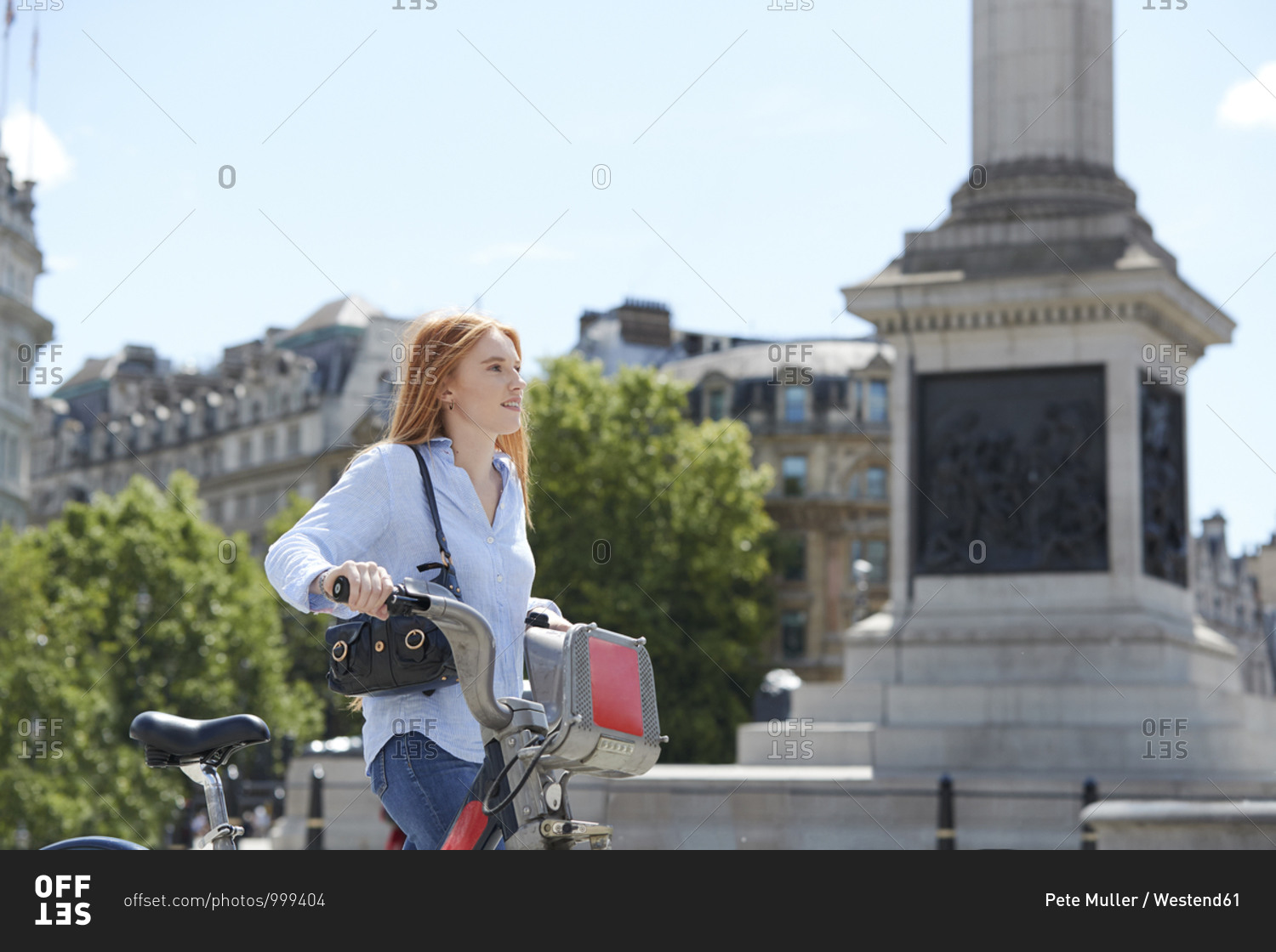 Thoughtful woman walking with hire bike in city during sunny day