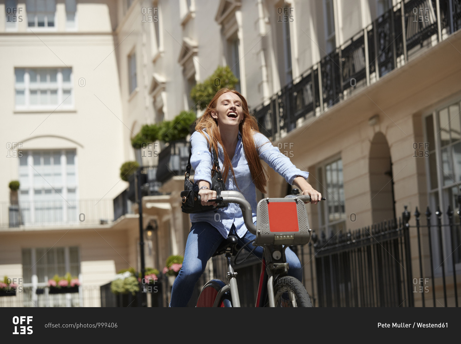 Cheerful woman riding hire bike in city during sunny day