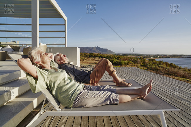 Senior couple lying on deck chairs at luxury beach house