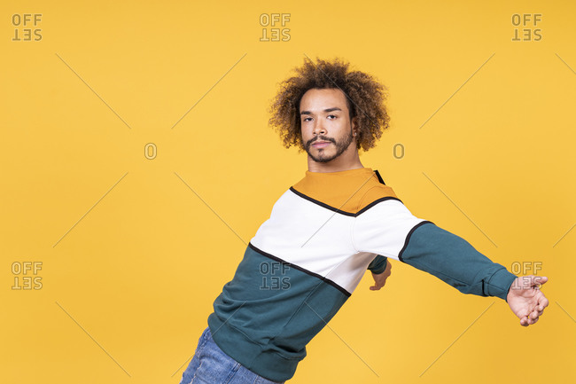 Cool young man with curly hair dancing against yellow background