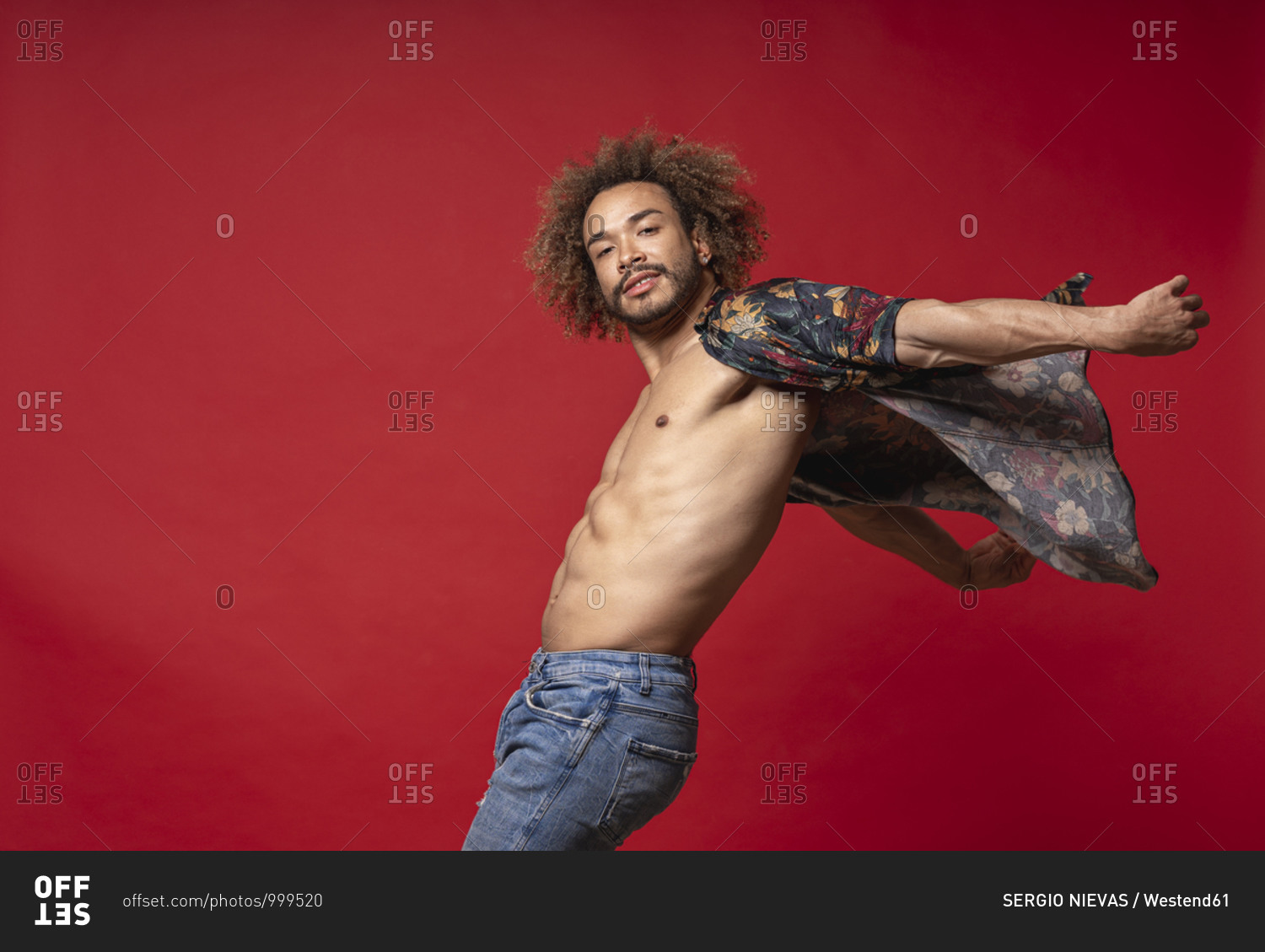 Young man wearing fully unbuttoned shirt dancing against red background