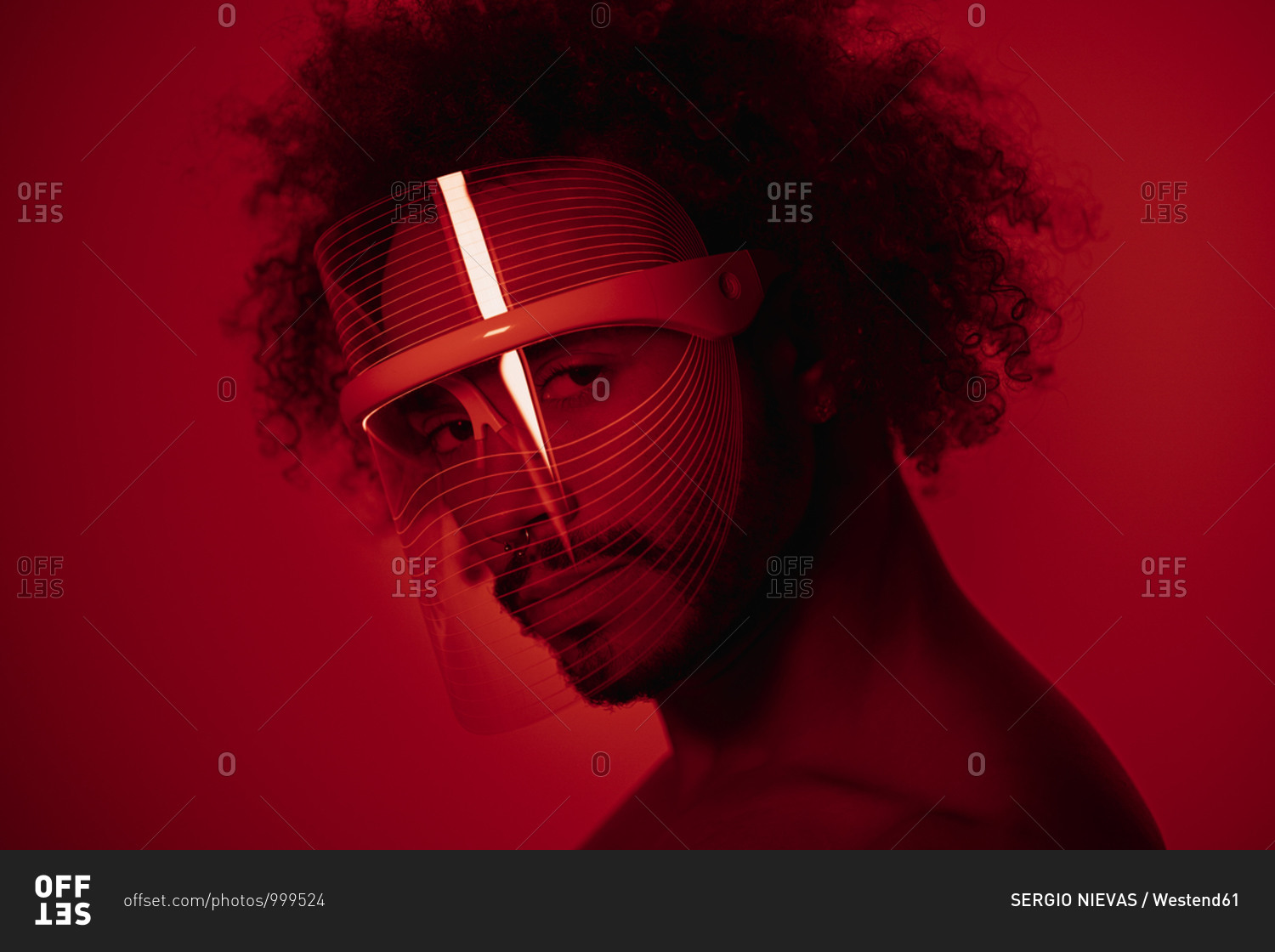 Close-up of young man wearing red led light mask against wall at home