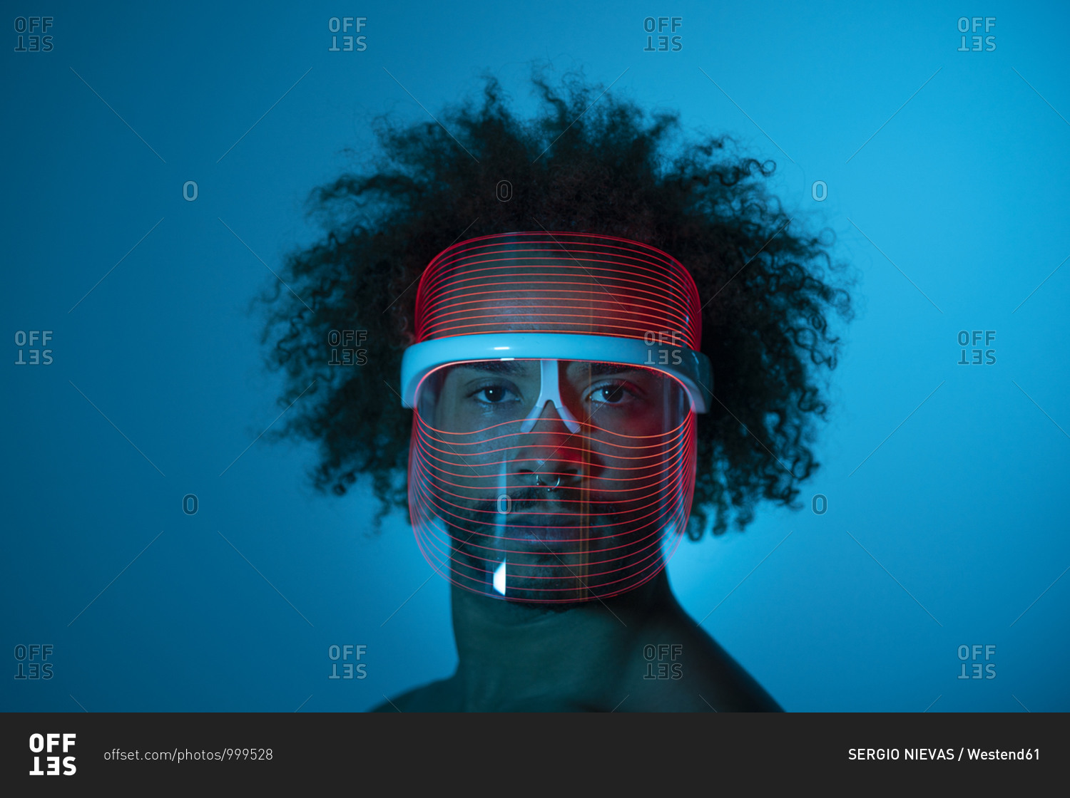 Serious young man wearing red led mask against wall at home