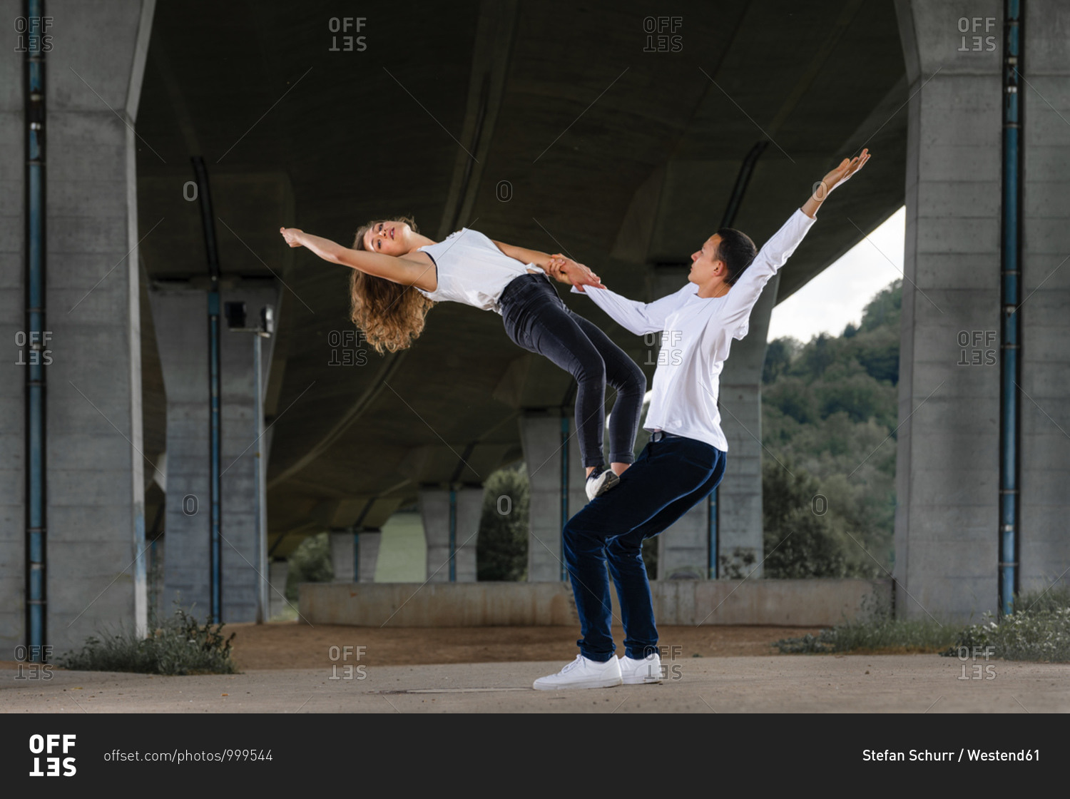 Male and female friends practicing aerobics on road under bridge