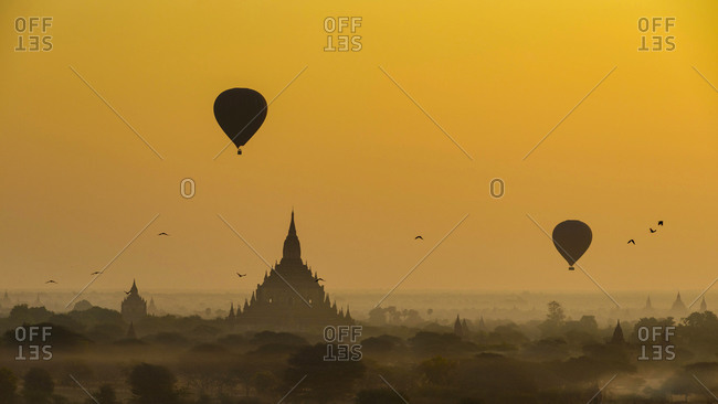 Myanmar- Mandalay Region- Bagan- Silhouettes of hot air balloons flying over ancient temples at foggy dawn