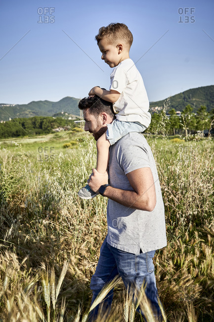 Father carrying son on shoulders while walking amidst plants against clear sky during sunny day