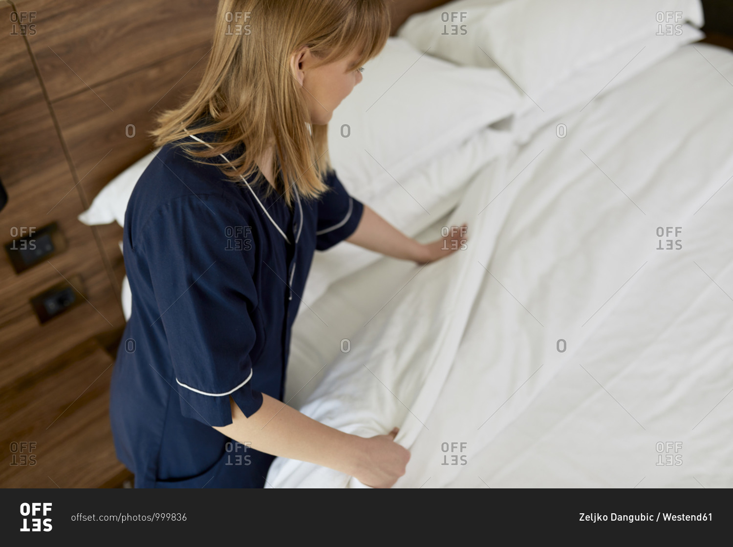Maid arranging duvet on bed in hotel room